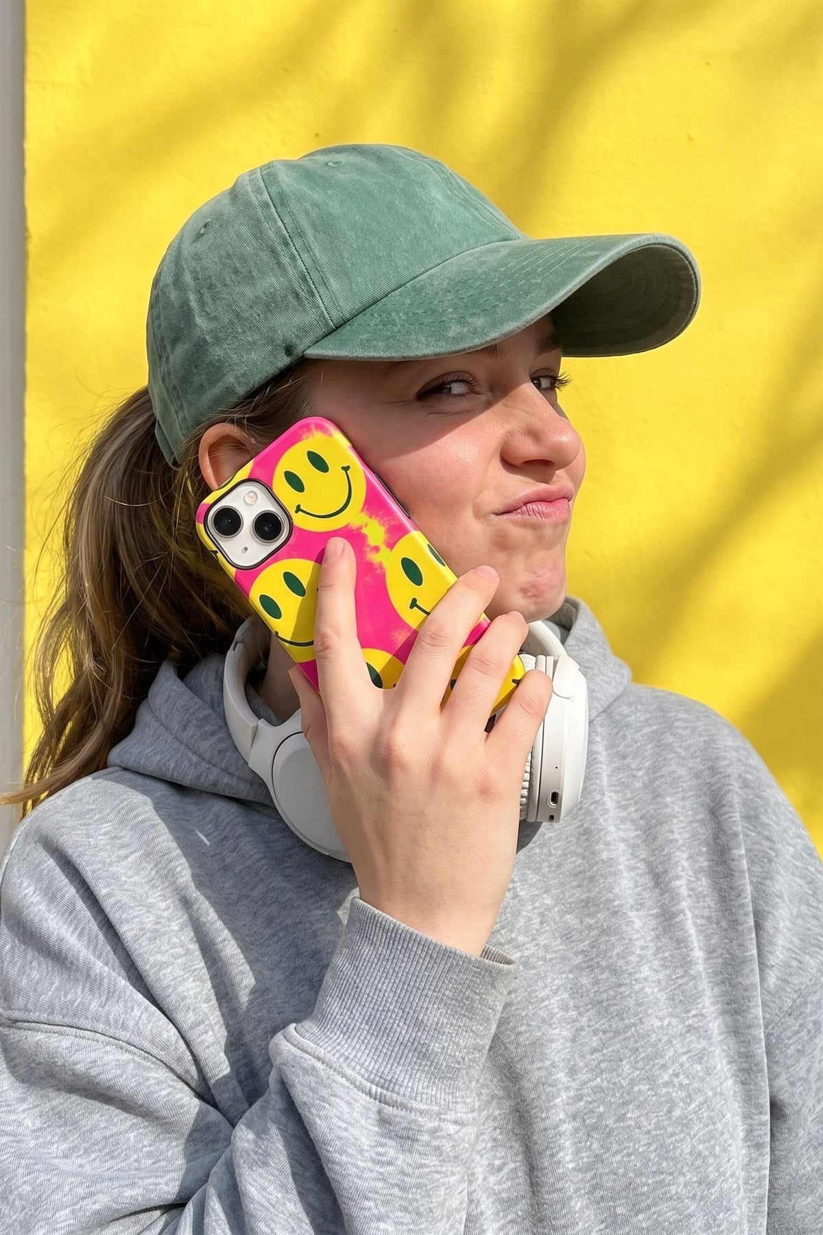 Vrouw met een groene pet belt met haar telefoon in het Fynne-hoesje Grin Reaper, voor een gele muur
