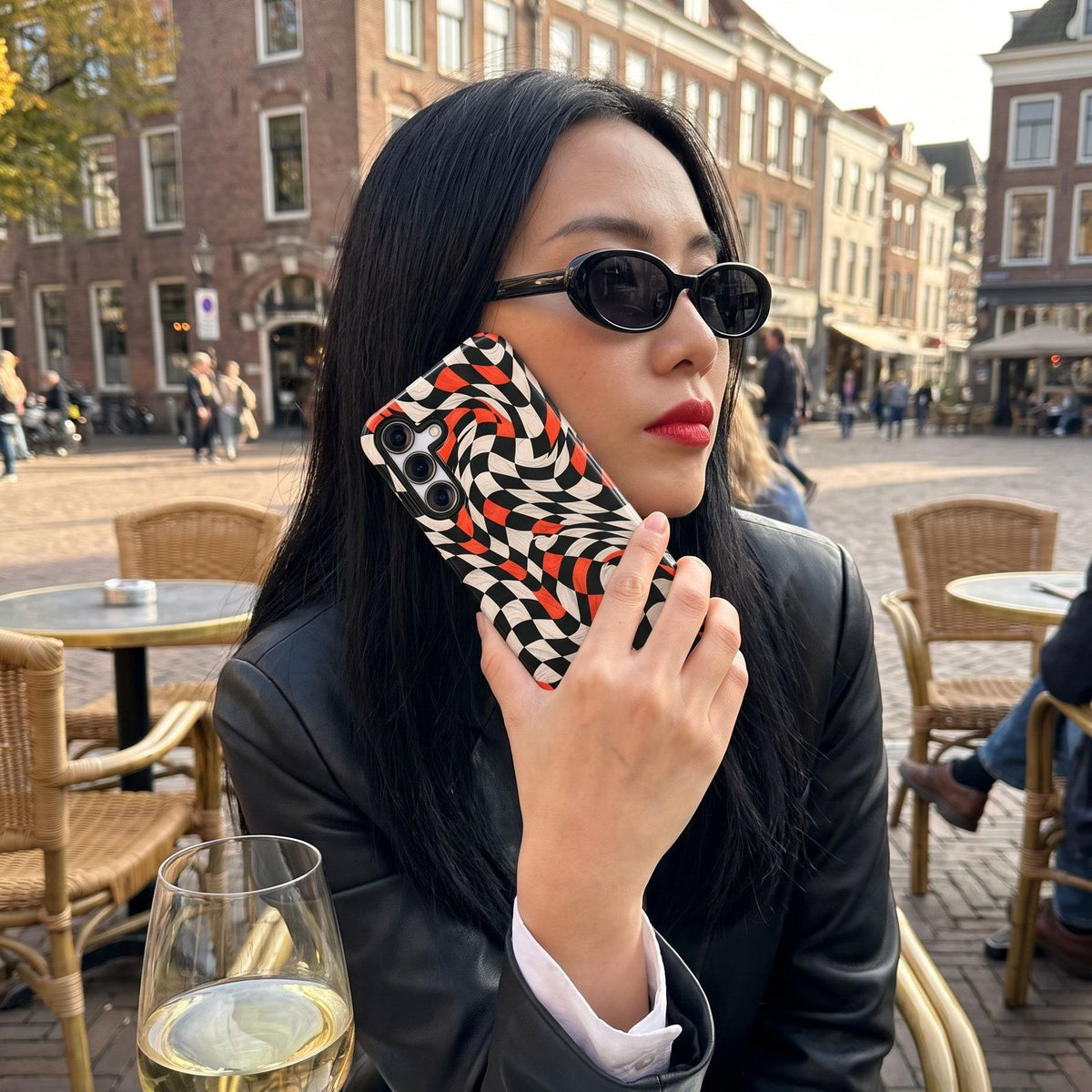 Vrouw met zonnebril op een terras in Utrecht houdt haar telefoon met het Fynne-hoesje Off Track tegen haar wang