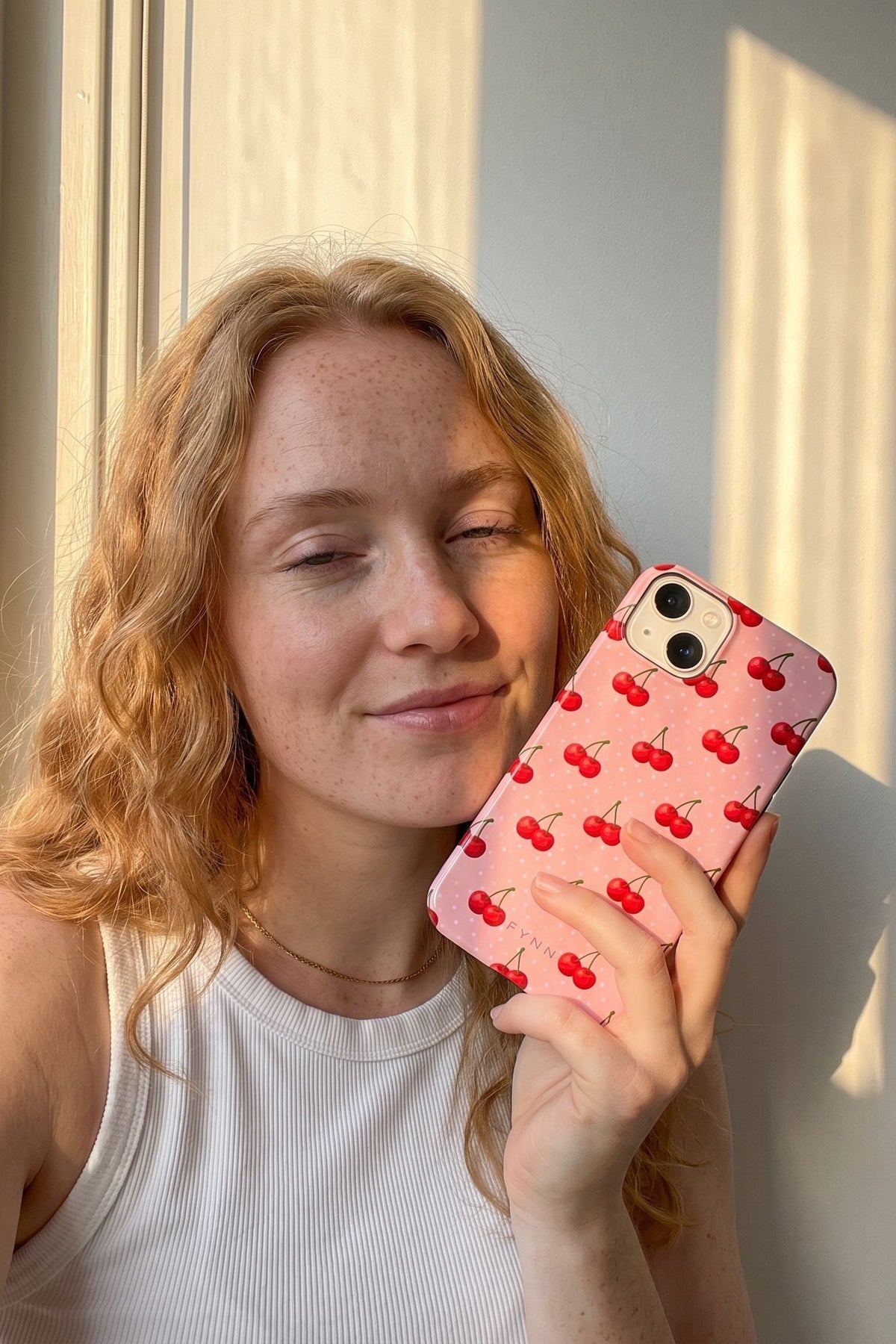 Vrouw met rood haar in de avondzon houdt haar telefoon met het kersenhoesje Double Trouble tegen haar wang