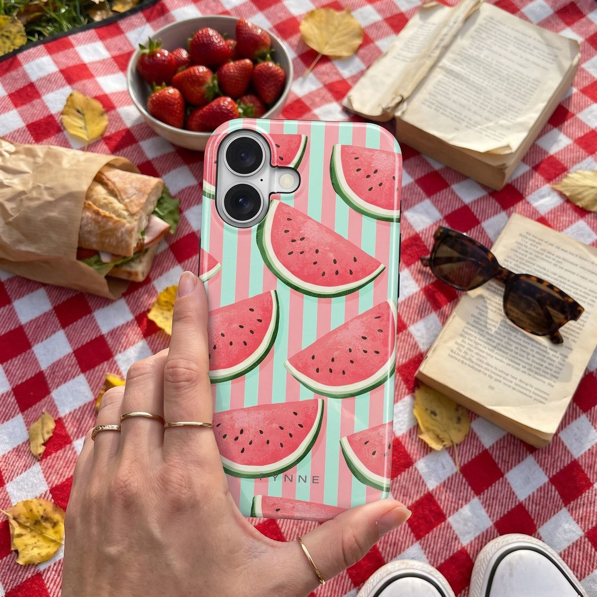 Telefoon met het watermeloenhoesje One in a Melon op een rood-wit geruit picknickkleed in het park