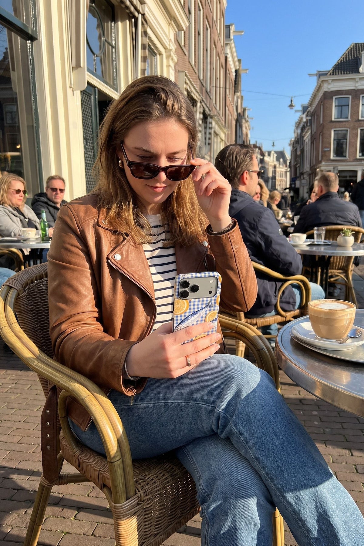 Vrouw op een terras schuift haar zonnebril omlaag en kijkt op haar telefoon met het Fynne-hoesje Fresh Catch