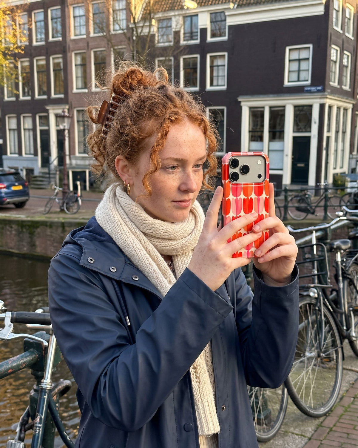 Vrouw met rood krullend haar maakt een foto aan de gracht met haar telefoon in het tulpenhoesje Tulip Mania