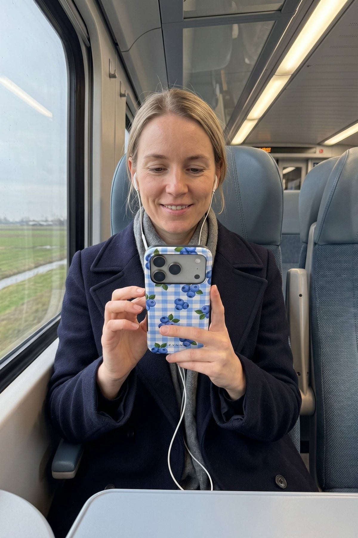 Vrouw in de trein kijkt op haar telefoon met het blauwe bosbessenhoesje Berry Sweet Picnic