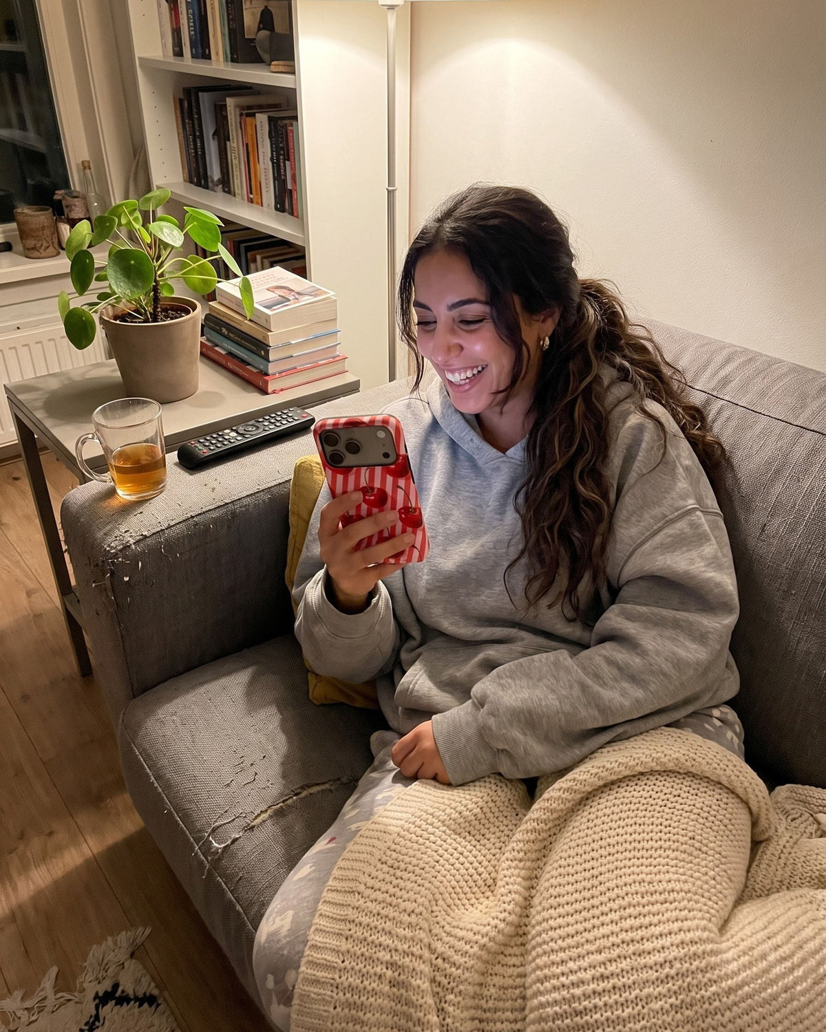 Vrouw op de bank lacht om iets op haar telefoon met het gestreepte kersenhoesje Cherry Picked