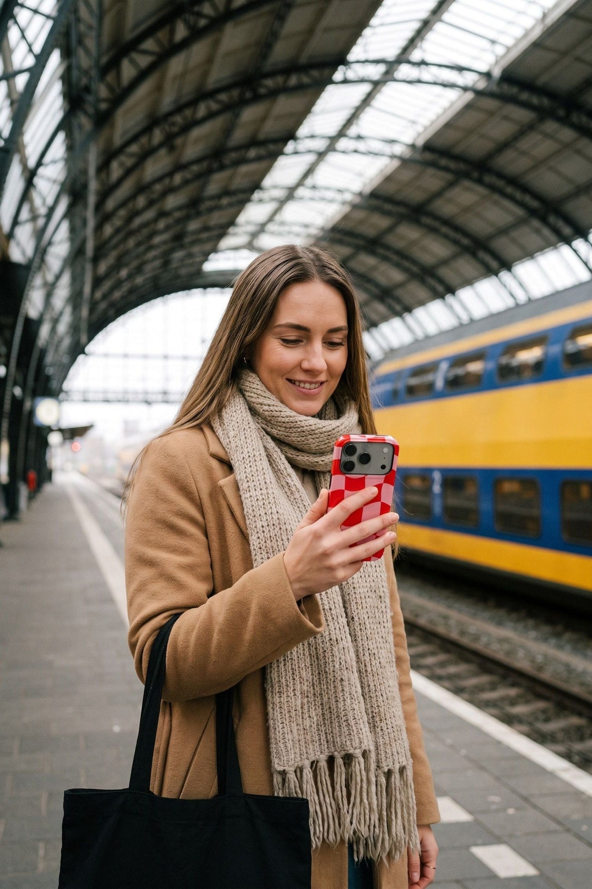 Vrouw op het perron van Amsterdam Centraal kijkt op haar telefoon met het rood-roze ruithoesje Check Mate